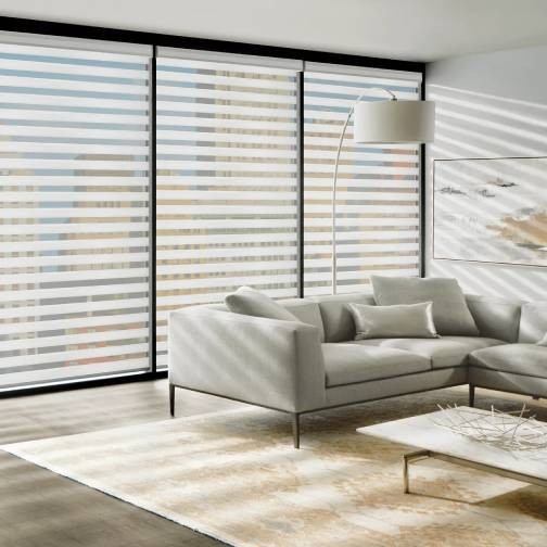Las cortinas con bandas blancas cubren una ventana ubicada detrás de un sofá gris y una mesa de café blanca